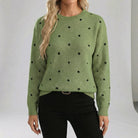 Green sweater with black polka dots worn by a person on a white background