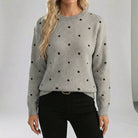 Person wearing a gray sweater with black polka dots against a plain background