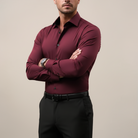 Man wearing a burgundy dress shirt and black pants against a beige background