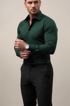 Man wearing a dark green dress shirt and black pants against a beige background