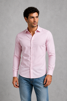 Man wearing a light pink dress shirt and blue jeans against a gray background