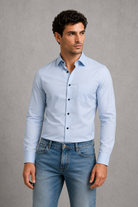 Man wearing a light blue shirt and jeans against a gray background