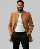 Man wearing a brown coat over a white shirt and dark pants on a gray background