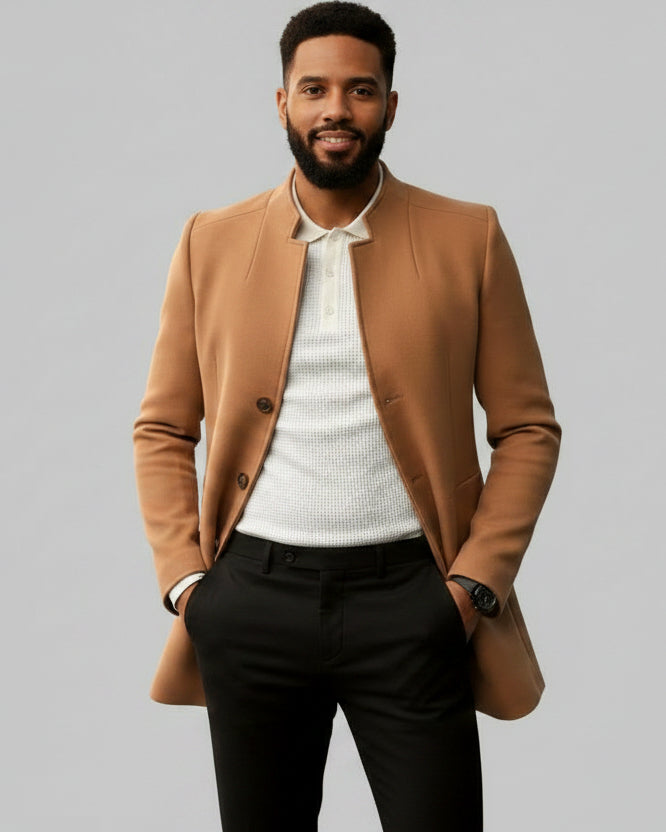 Man wearing a brown coat over a white shirt and dark pants on a gray background