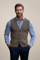 Man wearing a brown sweater vest over a blue checkered shirt on a beige background