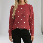 Red sweater with white polka dots worn by a person on a plain background