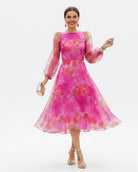 Woman wearing a vibrant pink floral dress standing on a street.