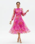 Woman wearing a vibrant pink floral dress standing on a street.