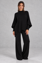 Women’s ribbed knit two-piece set with an asymmetric high-neck jumper, draped crossover hem and matching wide leg trousers.