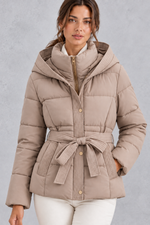 Women’s belted hooded quilted puffer jacket with warm padding, a high neckline, adjustable tie waist and practical side pockets.