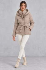 Women’s belted hooded quilted puffer jacket with warm padding, a high neckline, adjustable tie waist and practical side pockets.