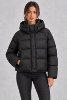 Women’s hooded puffer jacket with generous padding, a large hood, high protective neckline, long sleeves and relaxed silhouette.