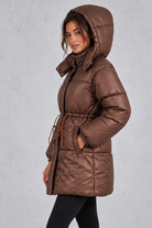 Women’s longline hooded puffer coat with quilted padding, a high neckline, adjustable drawstring waist and practical side pockets.