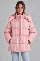 Women’s pink and white striped oversized hooded puffer jacket with horizontal quilting, a high stand collar and voluminous padded silhouette.