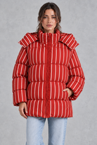 Women’s pink and white striped oversized hooded puffer jacket with horizontal quilting, a high stand collar and voluminous padded silhouette.