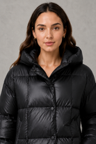 Women’s oversized hooded puffer jacket with a protective high collar, wide padded sleeves and a relaxed hip-length silhouette for winter layering.