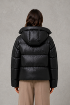 Women’s oversized hooded puffer jacket with a protective high collar, wide padded sleeves and a relaxed hip-length silhouette for winter layering.