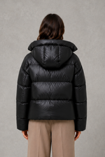 Women’s oversized hooded puffer jacket with a protective high collar, wide padded sleeves and a relaxed hip-length silhouette for winter layering.