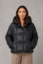 Women’s oversized hooded puffer jacket with a protective high collar, wide padded sleeves and a relaxed hip-length silhouette for winter layering.