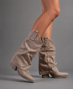 Women’s pointed toe knee high boots with a low chunky heel and relaxed Western-inspired shaft in a neutral shade.