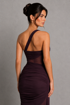 Woman wearing a dark purple dress with sheer back panels against a gray background