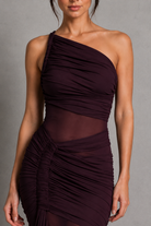 Woman wearing a dark purple one-shoulder dress against a gray background