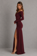 Woman wearing a burgundy off-shoulder gown with a slit on a gray background