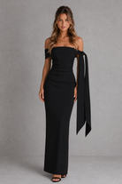 Woman wearing a black off-shoulder gown with a long train against a gray background