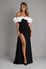 Woman wearing a black off-shoulder dress with white ruffles on a gray background