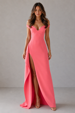 Woman wearing a pink evening gown with a high slit on a plain background
