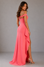 Woman wearing a pink off-shoulder gown with a slit on a gray background