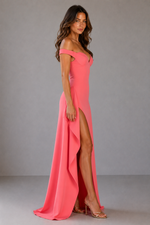 Woman wearing a pink off-shoulder dress with a high slit on a gray background