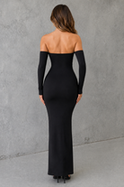 Woman wearing a black off-shoulder gown against a gray wall.