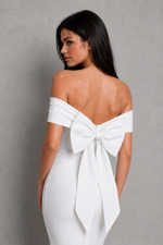 Woman wearing a white off-shoulder dress with a large bow detail on a gray background