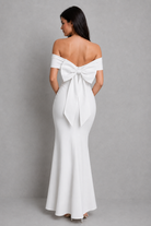 Woman wearing a white off-shoulder gown with a large bow detail on a gray background
