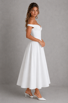 Woman wearing a white off-shoulder dress against a gray background