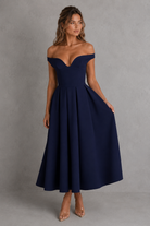 Woman wearing a navy off-shoulder dress against a gray background