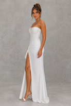 Woman wearing a strapless white gown with a high slit on a gray background