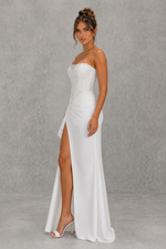 Woman wearing a strapless white gown with a high slit on a gray background