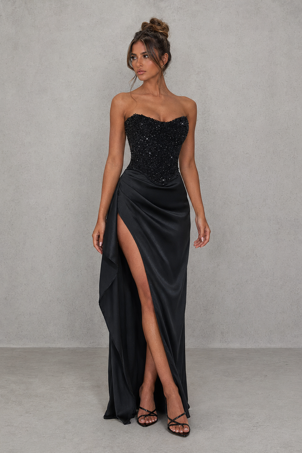Woman wearing a black strapless gown with a high slit on a gray background