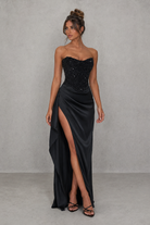 Woman wearing a black strapless gown with a high slit on a gray background