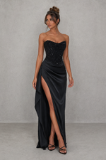 Woman wearing a black strapless gown with a high slit on a gray background