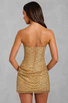 Woman wearing a gold strapless dress against a gray background