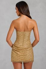 Woman wearing a gold strapless dress against a gray background