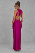 Woman wearing a vibrant pink evening gown with a open back design against a gray background