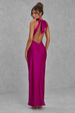 Woman wearing a vibrant pink evening gown with a open back design against a gray background