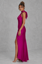 Woman wearing a vibrant pink evening gown with a high slit on a plain background