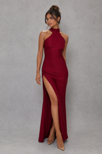 Woman wearing a burgundy halter neck gown with a high slit on a gray background