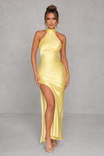 Woman wearing a yellow halter neck dress with a slit on a gray background