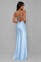 A woman modeling a light blue satin maxi dress from the back, featuring thin spaghetti straps, a tie-back neckline, and a floor-length flowing skirt, set against a neutral gray studio background.